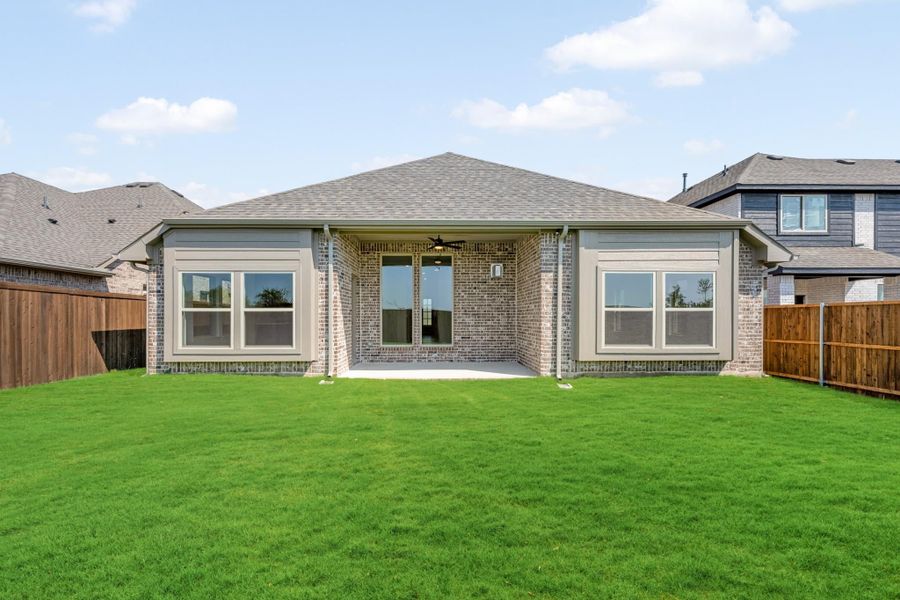 Rear exterior of single-story brick home with covered patio, large windows, and fenced backyard with green lawn