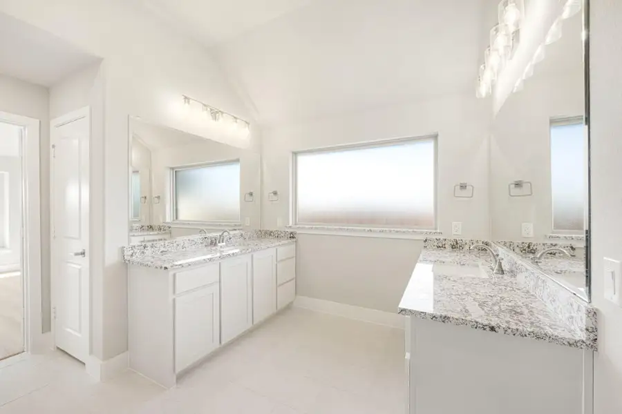 Bright master bathroom with dual vanities, granite countertops, white cabinets, and vaulted ceiling