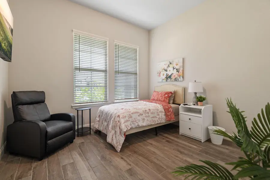 This cozy ADA=compliant bedroom features wood-look flooring, a large window for natural light, and neutral walls. It includes a twin bed, a comfortable recliner, and a white nightstand with a lamp, creating a welcoming and functional living space. This cozy ADA=compliant bedroom features wood-look flooring, a large window for natural light, and neutral walls. It includes a twin bed, a comfortable recliner, and a white nightstand with a lamp, creating a welcoming and functional living space.