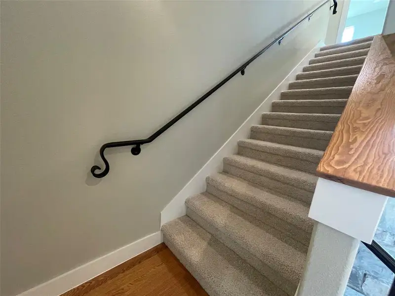 Carpeted staircase with a decorative wrought iron handrail and a light wood-finish newel post cap