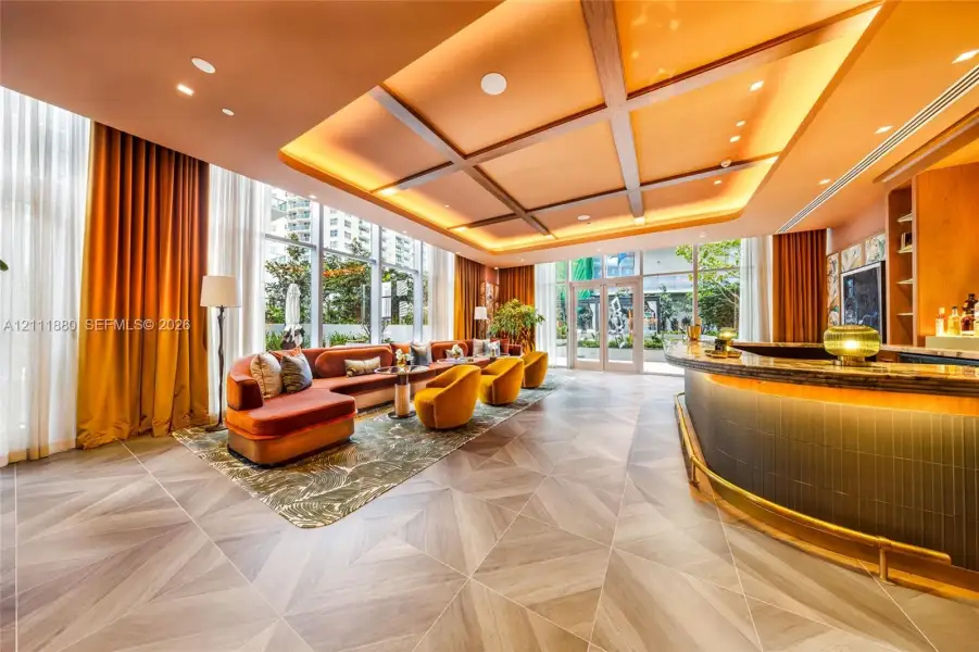 Coffered ceiling with recessed lighting, floor-to-ceiling windows, geometric wood-finish tile flooring, and a curved built-in bar with a stone countertop