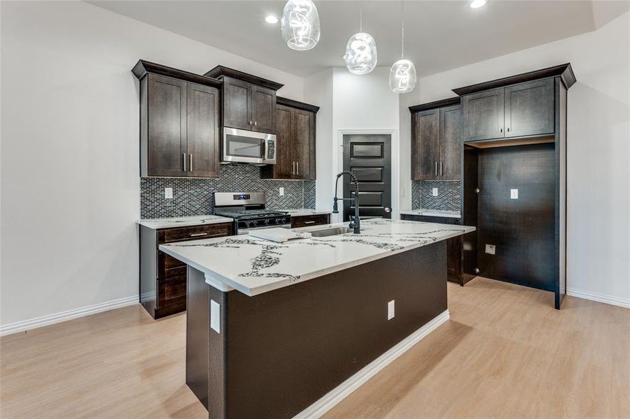 Kitchen featuring a kitchen island with sink, light wood-type flooring, pendant lighting, sink, and appliances with stainless steel finishes