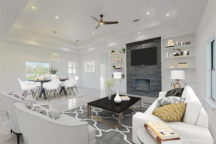 Living room with built in features, a fireplace, ceiling fan, and a raised ceiling