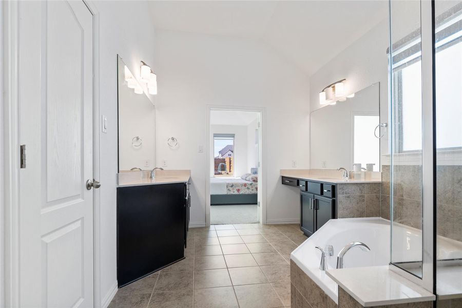 Vast tile flooring connects dual vanities and a deep corner tub in this bright primary bath. Vast tile flooring connects dual vanities and a deep corner tub in this bright primary bath.