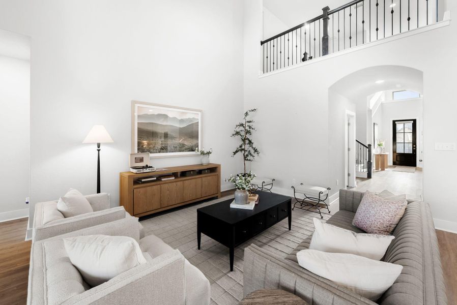 A spacious living area features high ceilings and rich wood flooring, connecting seamlessly to an open hallway.