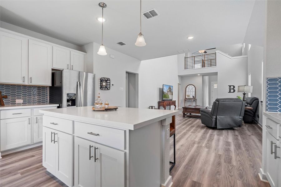 Kitchen with stainless steel refrigerator with ice dispenser, light wood finished floors, a kitchen island, light countertops, and backsplash Kitchen with stainless steel refrigerator with ice dispenser, light wood finished floors, a kitchen island, light countertops, and backsplash