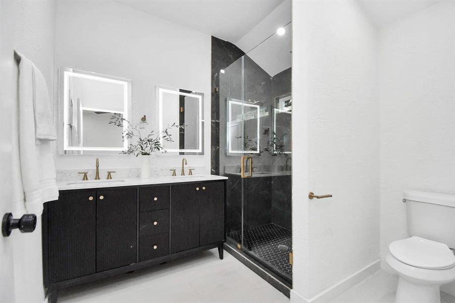 This is a modern bathroom with grey marble tiles and includes a rainfall showerhead, sleek metal fixtures, and a large mirror with integrated lighting. A recessed shelf provides convenient storage.