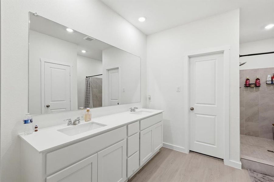 Bathroom featuring a dual vanity with white cabinetry and integrated sinks, a large wall-mounted mirror, recessed lighting, and light wood-finish flooring Bathroom featuring a dual vanity with white cabinetry and integrated sinks, a large wall-mounted mirror, recessed lighting, and light wood-finish flooring