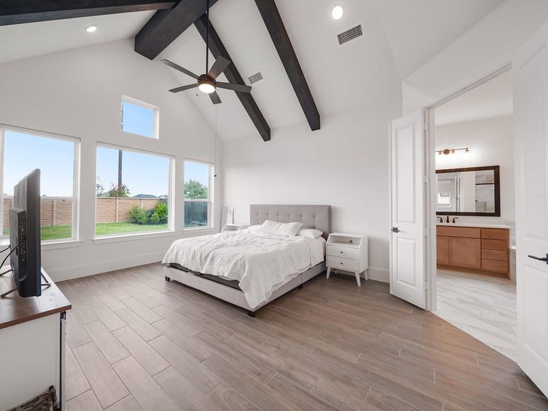Your retreat awaits—this expansive primary suite features vaulted ceilings with rustic beams, large windows with backyard views, and plenty of space for a seating area or reading nook.