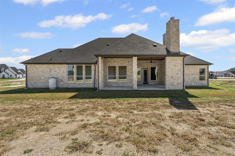 Back of property featuring a patio, a lawn, a chimney, and roof with shingles