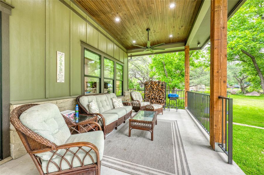 Covered porch featuring a wood-finish ceiling with recessed lighting and a ceiling fan, robust wood support beams, a stone knee wall, and a metal railing system