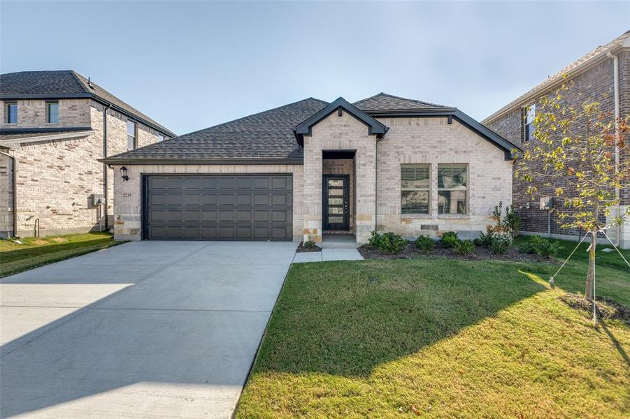 French country home featuring brick siding, roof with shingles, a front lawn, and driveway