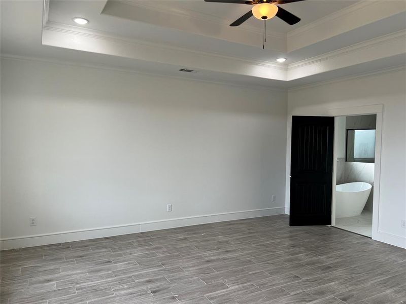Unfurnished bedroom with a raised ceiling, recessed lighting, wood finish floors, a ceiling fan, and crown molding