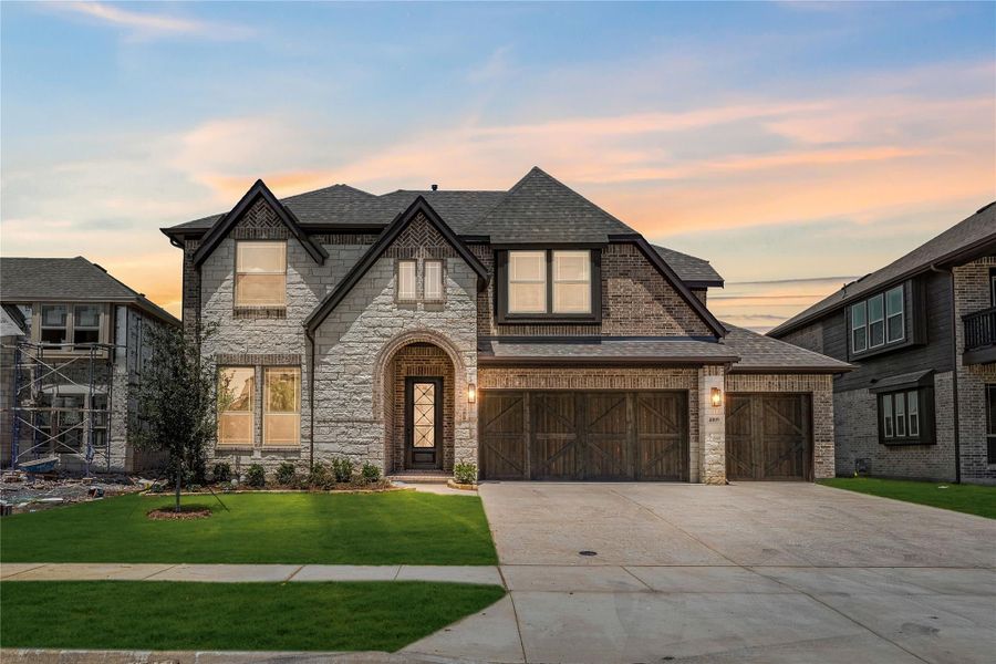 Two-story home with stone and brick exterior, arched entry, two-car garage, and green front lawn at dusk