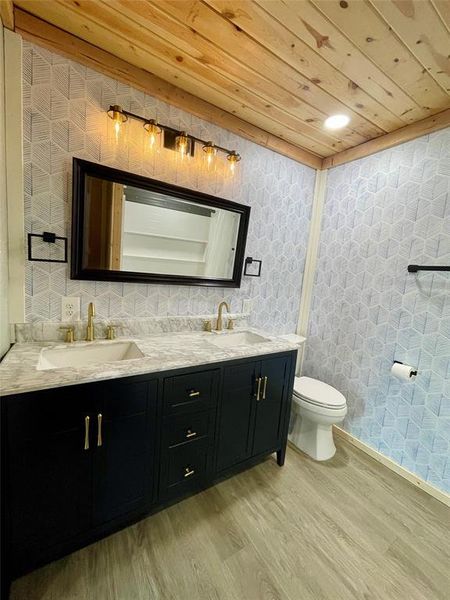 Bathroom featuring double vanity, wood ceiling, and decorative wallpaper