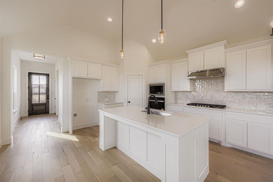 Kitchen featuring tasteful backsplash, white cabinetry, light stone countertops, a kitchen island with sink, and light wood-style flooring Kitchen featuring tasteful backsplash, white cabinetry, light stone countertops, a kitchen island with sink, and light wood-style flooring