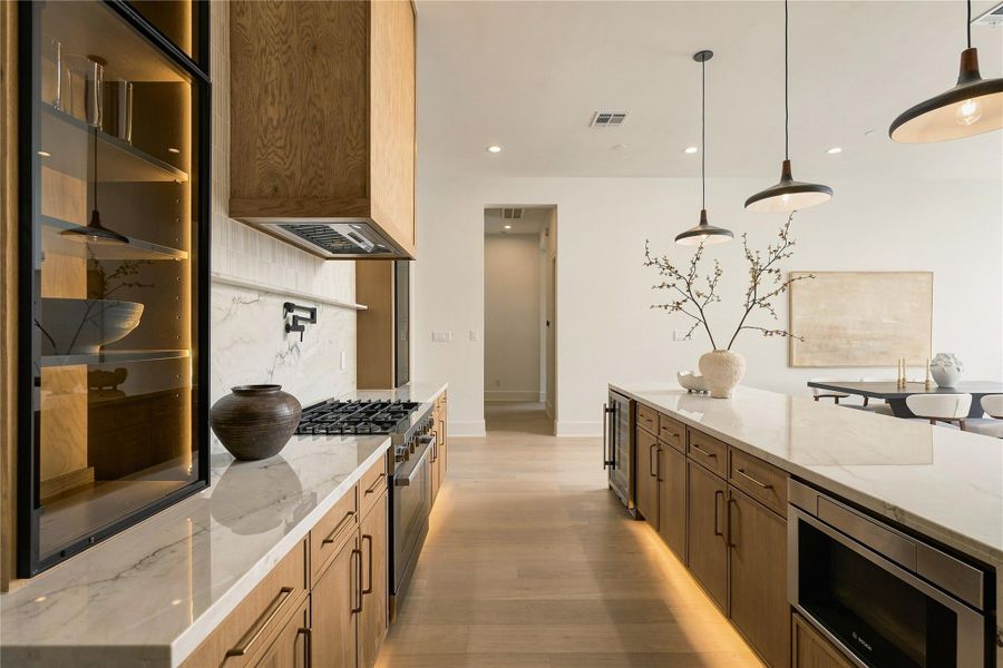 A dramatic perspective showcases the kitchen’s Midnight Glass Towers and illuminated cabinetry, creating a striking contrast against the warmth of the white oak finishes