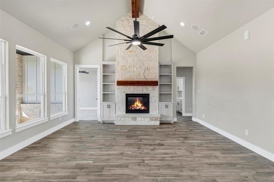 Unfurnished living room with a stone fireplace, wood-type flooring, lofted ceiling with beams, built in features, and ceiling fan