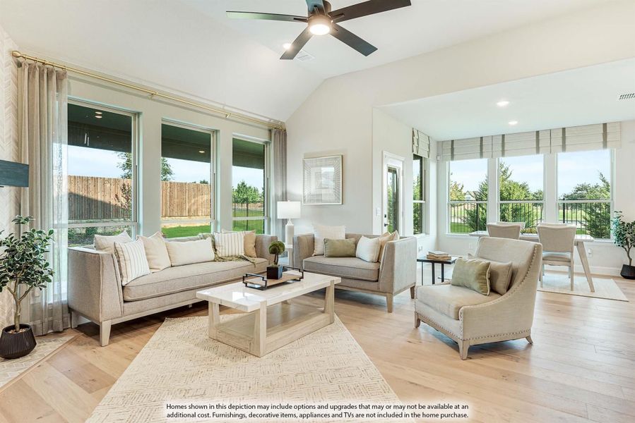 Bright living room with vaulted ceiling, ceiling fan, hardwood floors, and large windows overlooking backyard
