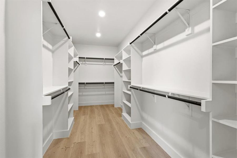 The walk-in closet features ample shelving, hanging rods, recessed lighting, and light-toned flooring