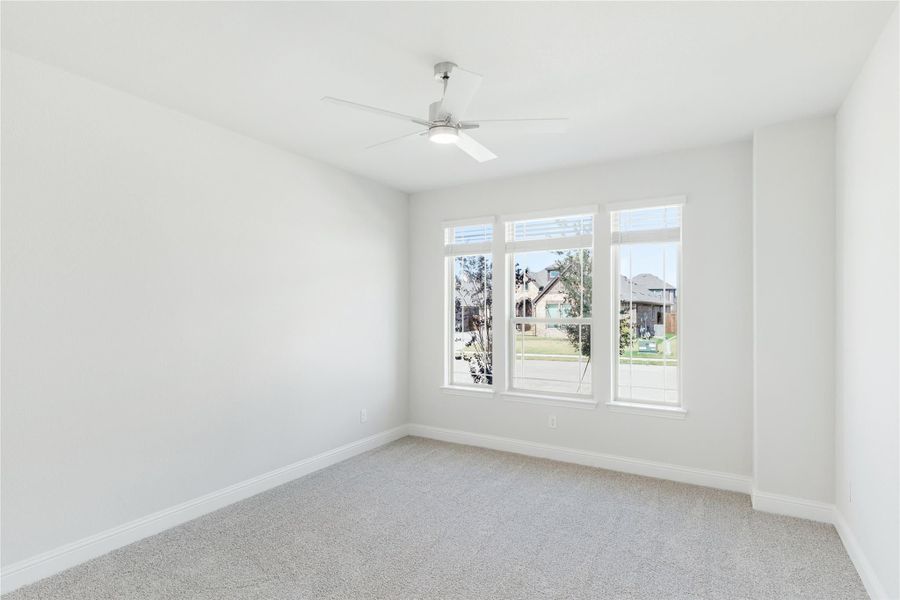 Empty bedroom with carpet flooring, ceiling fan, and three large windows with neighborhood view