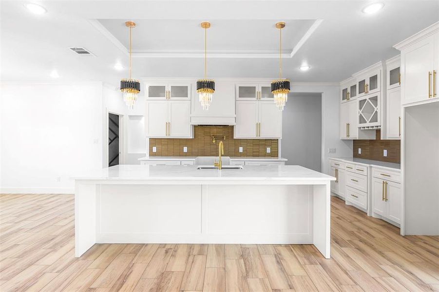 Kitchen featuring a tray ceiling, light wood finished floors, light stone countertops, decorative backsplash, and crown molding