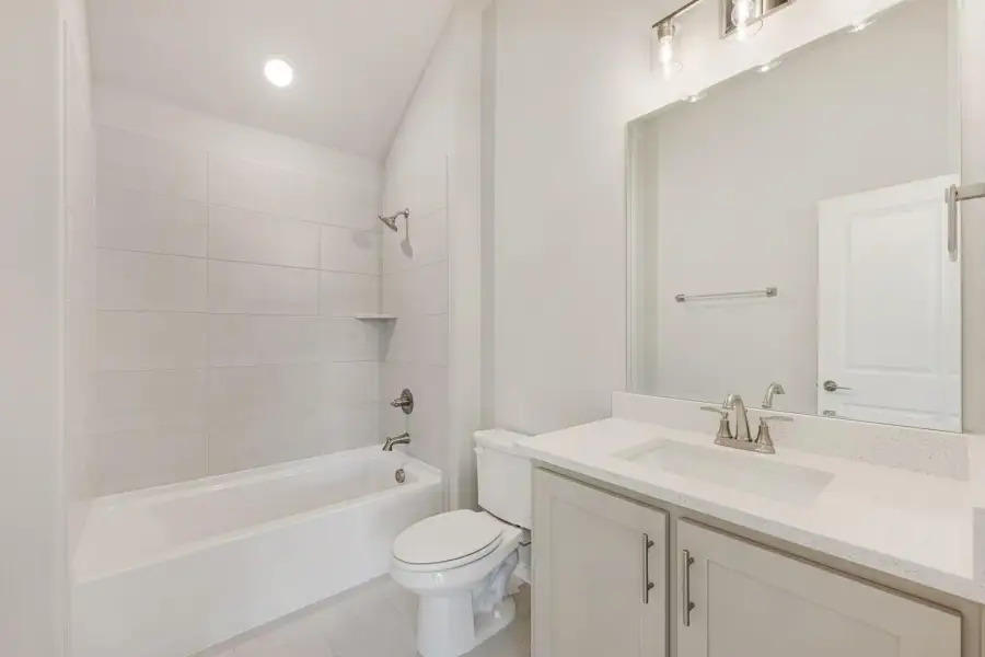 Full bathroom with tiled tub-shower combo, white vanity with quartz countertop, and large mirror