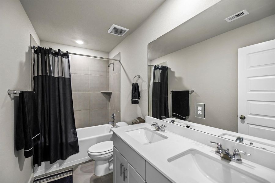 Modern bathroom featuring a double vanity, sleek fixtures, and a tiled shower area with a bathtub.