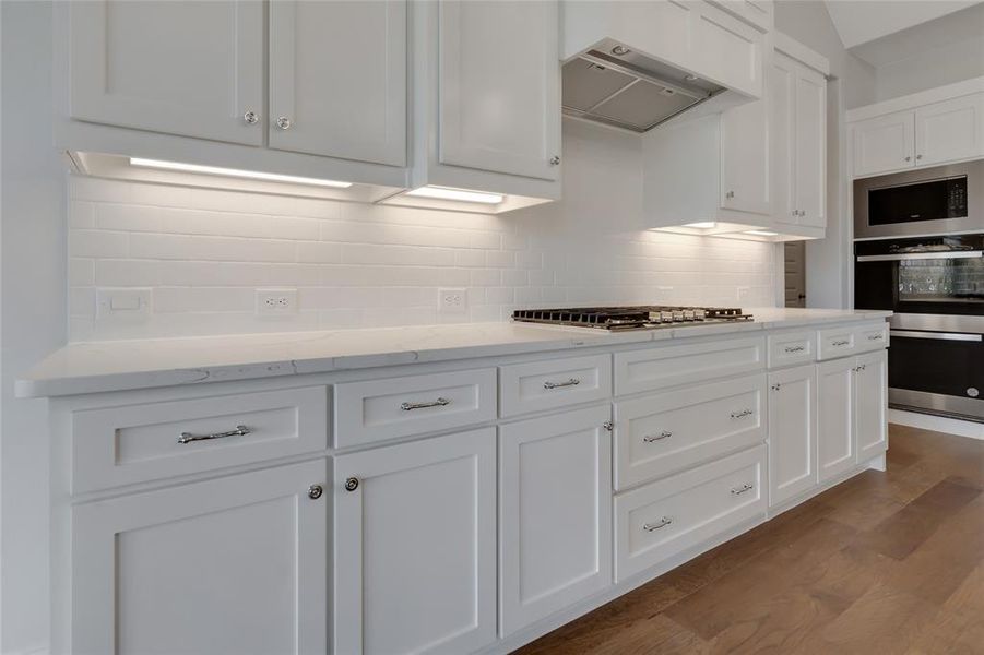 Kitchen with wall chimney exhaust hood, decorative backsplash, light hardwood / wood-style floors, white cabinetry, and stainless steel appliances