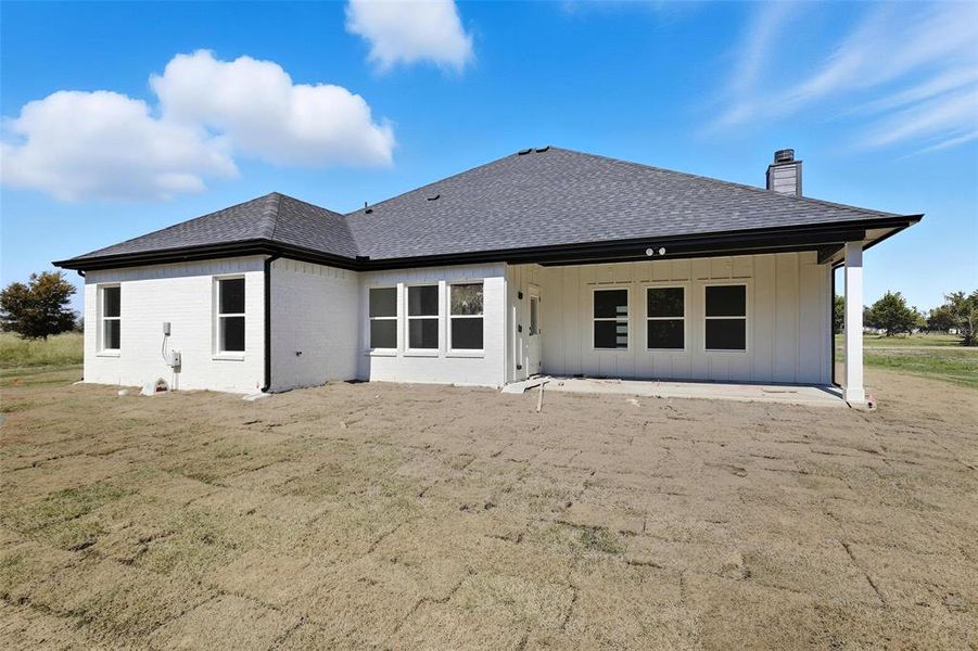 Rear view of house with a chimney, a shingled roof, a patio area, board and batten siding, and brick siding Rear view of house with a chimney, a shingled roof, a patio area, board and batten siding, and brick siding
