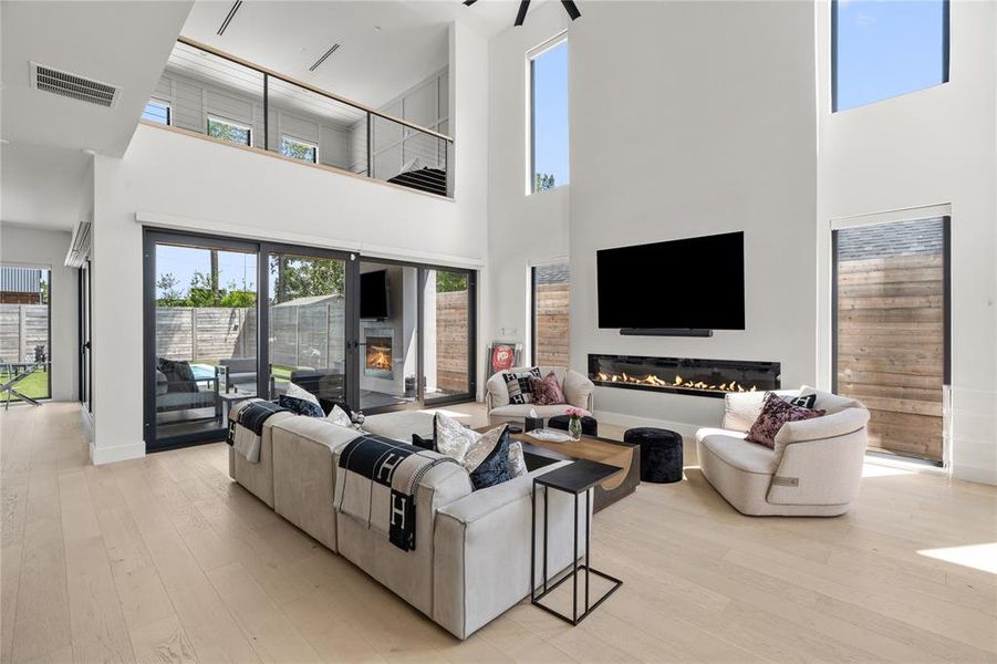 Living room with fireplace, grand stairway, light wood flooring, and custom electric shades