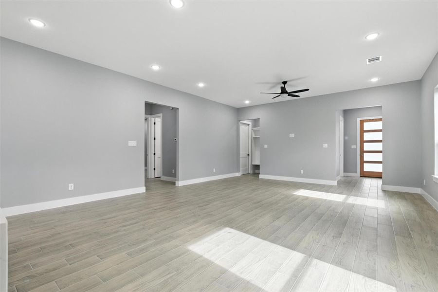 This spacious living area features modern gray walls, recessed lighting, and light flooring. It includes a ceiling fan and offers access to adjacent rooms and a contemporary wooden front door, creating a welcoming and open atmosphere.