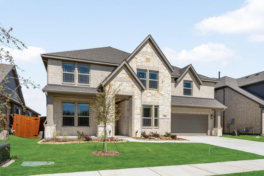 Two-story home with stone and brick exterior, two-car garage, and landscaped front yard
