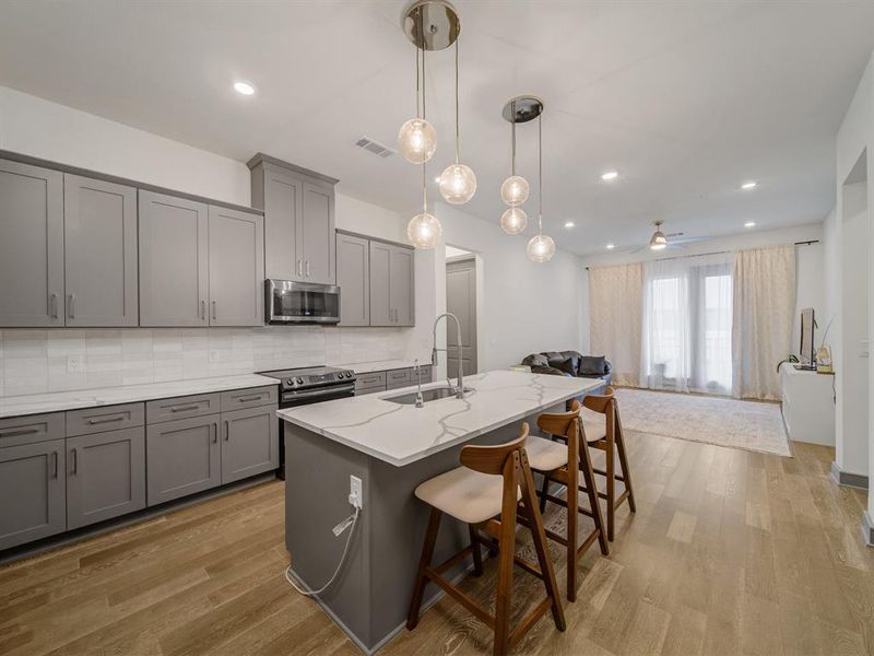Kitchen featuring gray cabinets, decorative backsplash, a kitchen island with sink, light wood-style floors, and recessed lighting