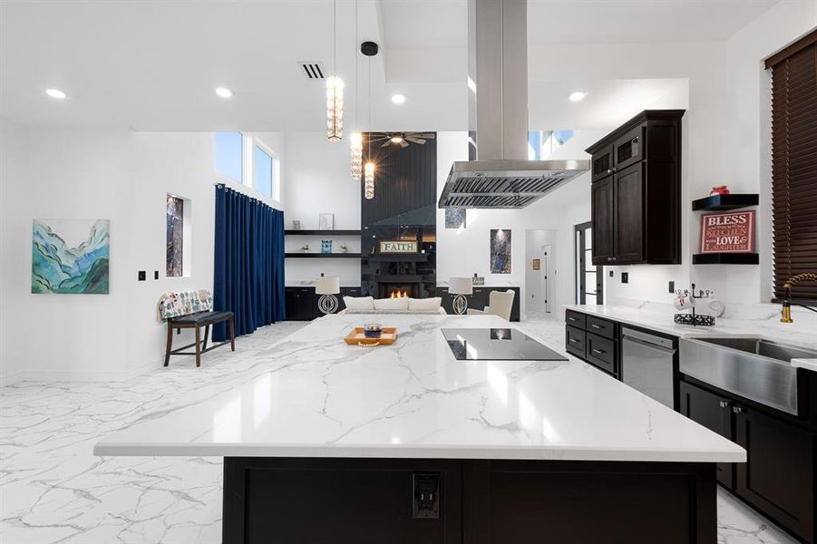 Kitchen featuring dark cabinets, light marble finish flooring, light stone countertops, a fireplace, and open floor plan