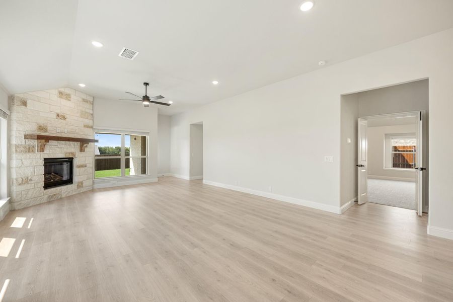 Open living room with stone fireplace, light wood floors, and ceiling fan