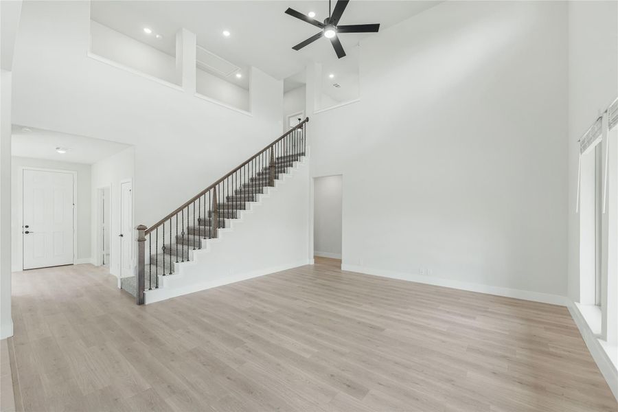 Open living area with two-story ceiling, staircase with iron balusters, ceiling fan, and light hardwood floors