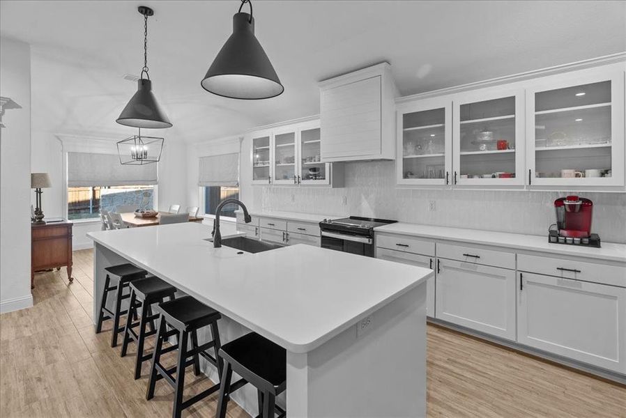 Kitchen with light wood finished floors, a center island with sink, a kitchen breakfast bar, electric stove, and a sink