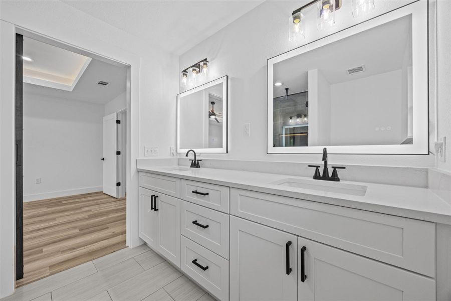 Dual vanities featuring white shaker-style cabinetry, quartz countertops, back lit mirrors, and matte black hardware Dual vanities featuring white shaker-style cabinetry, quartz countertops, back lit mirrors, and matte black hardware
