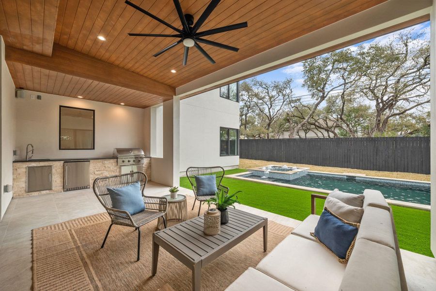 Fenced backyard featuring an outdoor kitchen and area to lounge, a patio, a ceiling fan, and a pool with connected hot tub