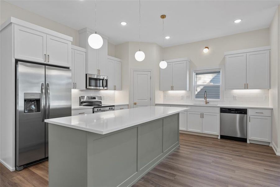 Kitchen featuring stainless steel appliances, backsplash, white cabinetry, hanging light fixtures, and dark wood-type flooring Kitchen featuring stainless steel appliances, backsplash, white cabinetry, hanging light fixtures, and dark wood-type flooring