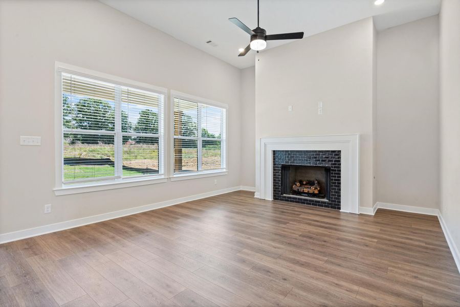 Living area featuring a fireplace with dark tile surround and white mantel, wood-finish flooring, vaulted ceiling, and multiple windows Living area featuring a fireplace with dark tile surround and white mantel, wood-finish flooring, vaulted ceiling, and multiple windows