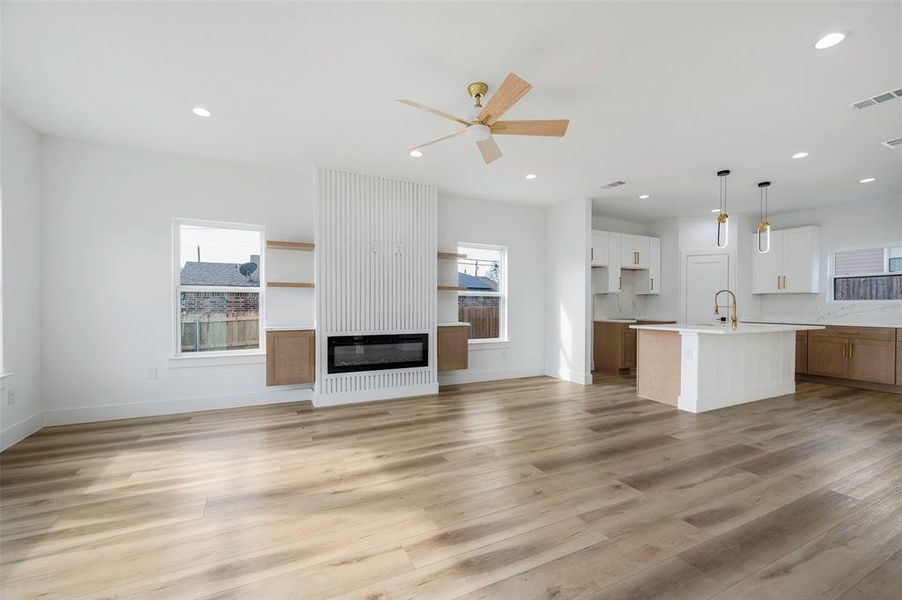 Unfurnished living room featuring ceiling fan, a large fireplace, light wood-type flooring, and sink