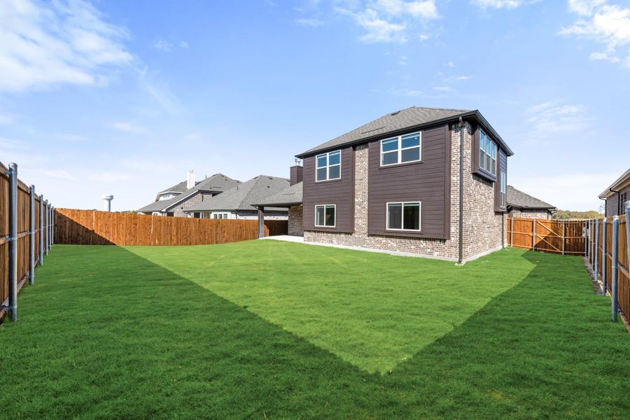 Two-story brick and dark siding home with large fenced backyard and green lawn