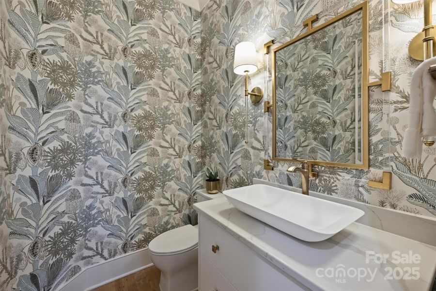 Guests can enjoy this charming half bath on the main level, featuring designer wallpaper, elegant light fixtures, and a stunning vanity with quartz countertops.