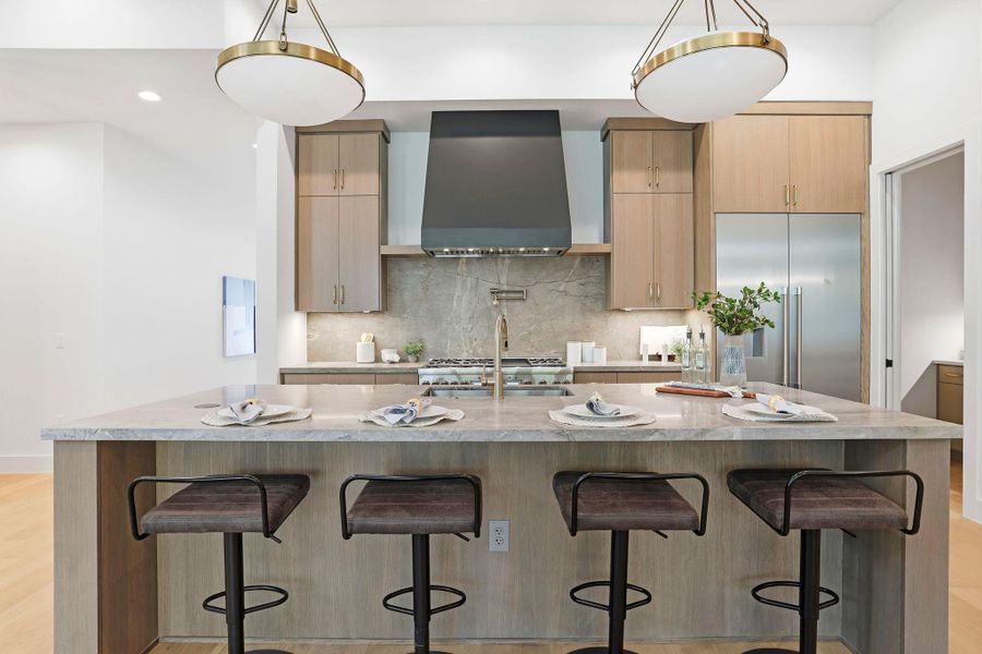 Kitchen with light brown cabinetry, modern cabinets, light stone counters, stainless steel built in refrigerator, and a kitchen breakfast bar