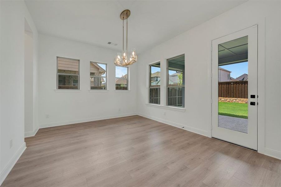 Open interior space featuring wood-finish flooring, white walls, and a contemporary chandelier Open interior space featuring wood-finish flooring, white walls, and a contemporary chandelier