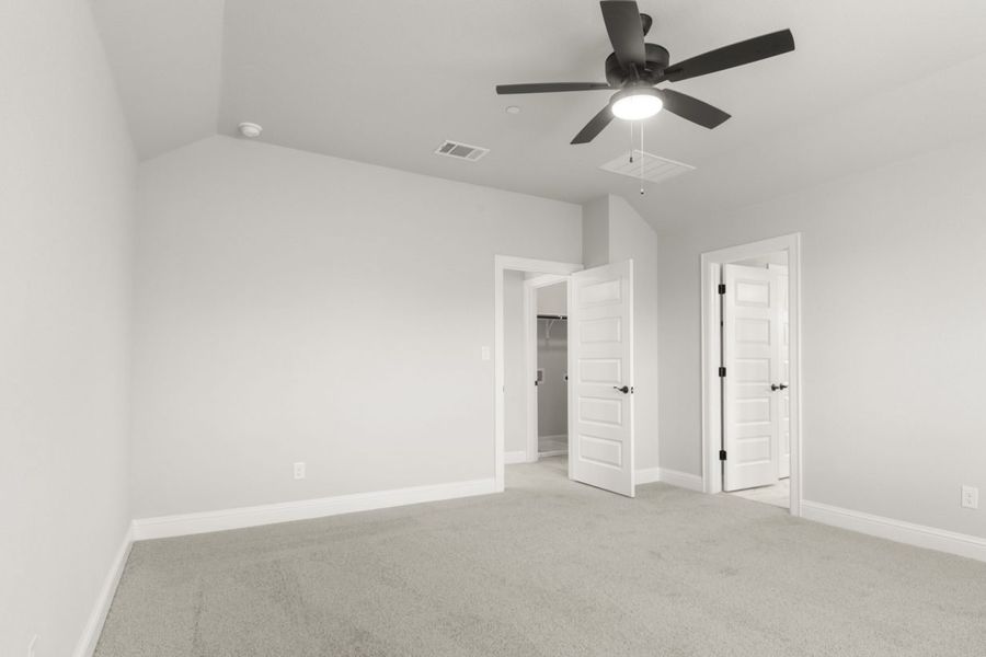 The primary bedroom with tan carpet, white walls, white doors, and a black ceiling fan.