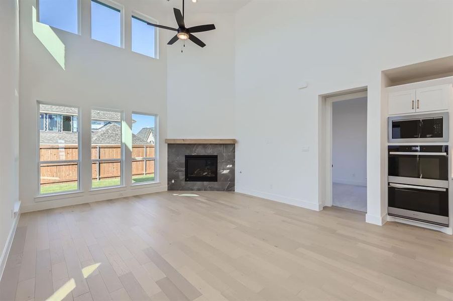 Unfurnished living room with a tiled fireplace, a high ceiling, light wood-type flooring, and ceiling fan