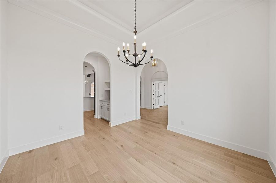 Spacious room featuring wood-finish flooring, a contemporary chandelier, arched entryways, and crisp white baseboards